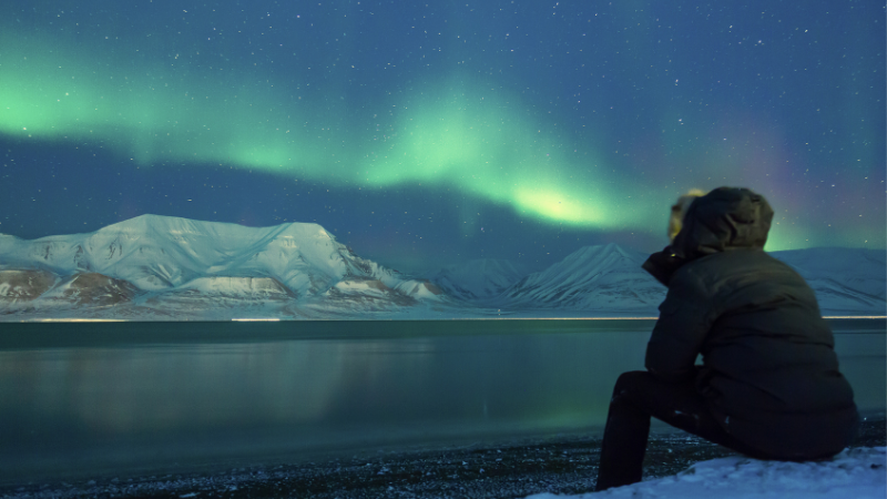 アラスカで座ってオーロラを眺める女性